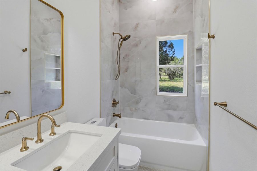 Bathroom featuring a white vanity with a light-colored countertop, gold-toned fixtures, a framed mirror, and a white bathtub with tile surround Bathroom featuring a white vanity with a light-colored countertop, gold-toned fixtures, a framed mirror, and a white bathtub with tile surround
