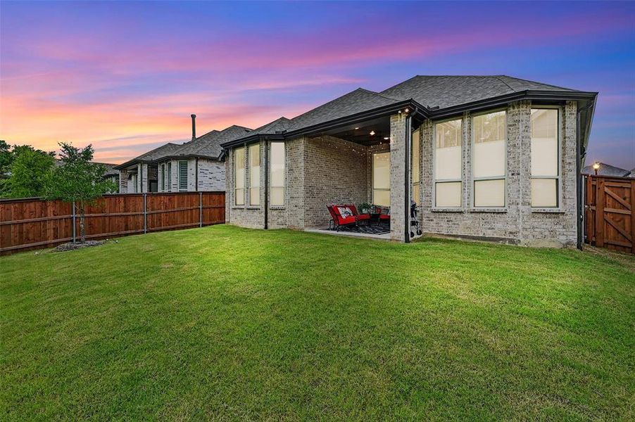 Back of property at dusk featuring a fenced backyard, brick siding, a patio area, and roof with shingles Back of property at dusk featuring a fenced backyard, brick siding, a patio area, and roof with shingles