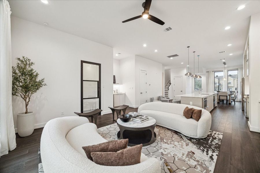 Inviting living space anchored by a sleek fireplace feature wall and custom built-ins, all set beneath high ceilings with recessed lighting. The open design effortlessly transitions into the kitchen and dining areas, reinforcing the home’s cohesive flow. Expansive rear windows capture serene outdoor views, creating a light-filled environment perfect for relaxing or hosting gatherings.