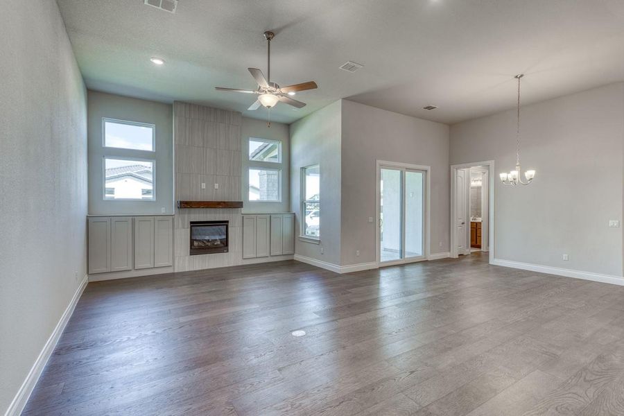 Unfurnished living room with a tile fireplace, ceiling fan, wood finished floors, and a chandelier