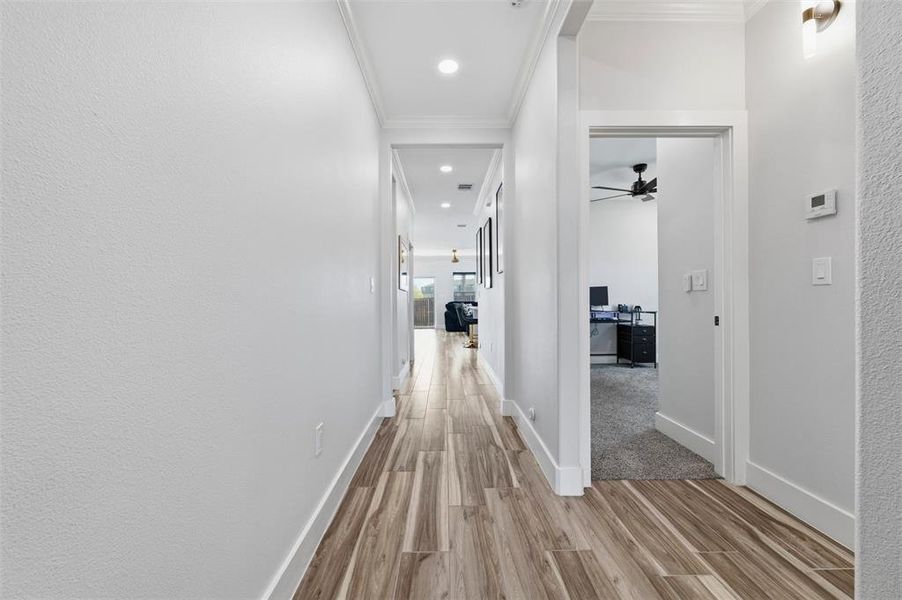 Hall with light wood finished floors, crown molding, and recessed lighting