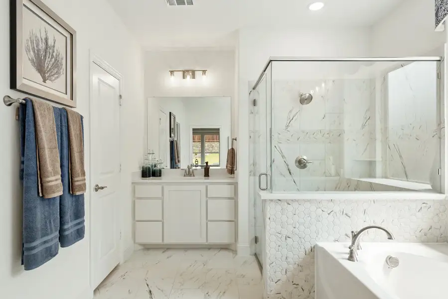 Bathroom with white vanity, glass-enclosed shower, soaking tub, and marble tile floors and walls