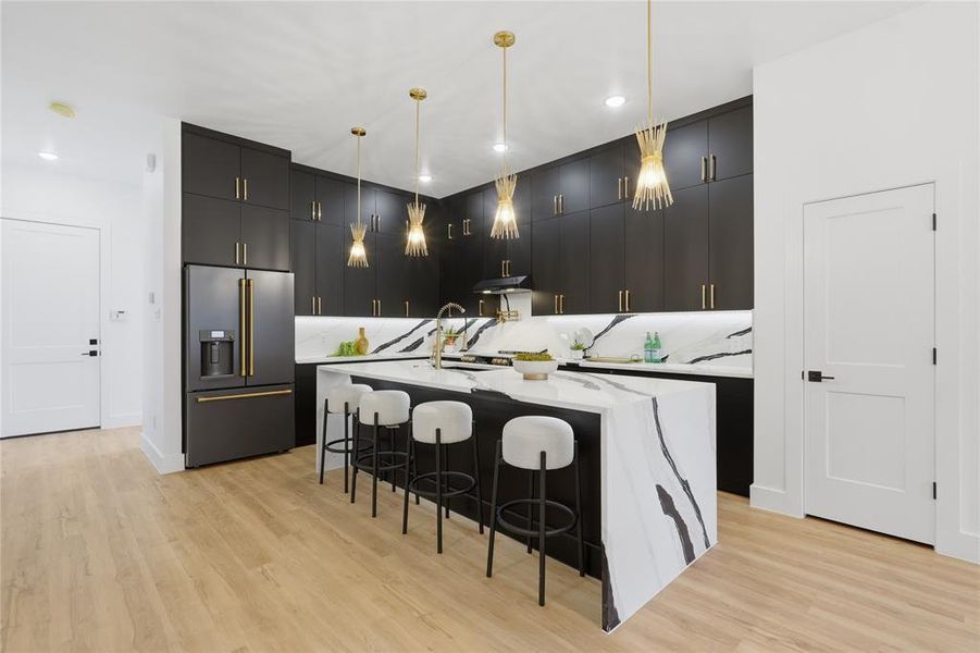 Kitchen with pendant lighting, high end refrigerator, an island with sink, dark cabinetry, and light stone counters