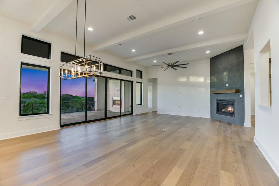 Living room featuring a tile fireplace, light wood-style flooring, a ceiling fan, suspended lighting, and lofted ceiling