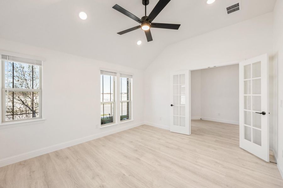 Empty bedroom with light wood floors, black ceiling fan, and white French doors