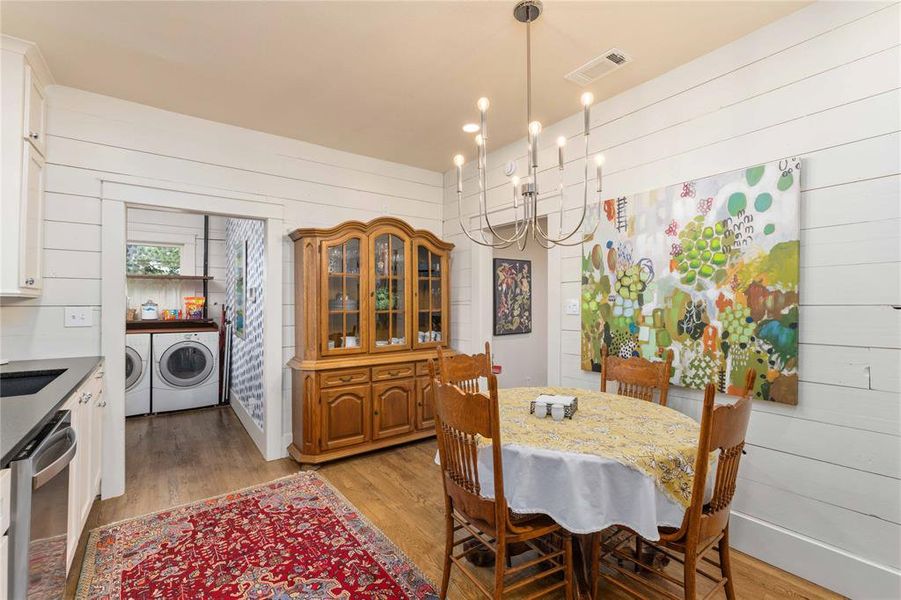 Dining area featuring wood-finish flooring, shiplap walls, and a contemporary chandelier