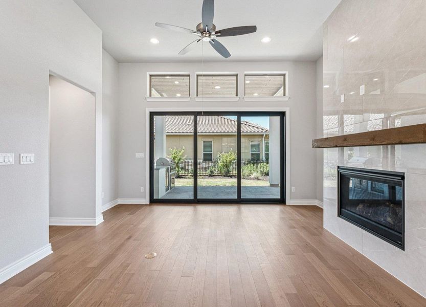 Unfurnished living room with a ceiling fan, wood finished floors, a fireplace, and a towering ceiling