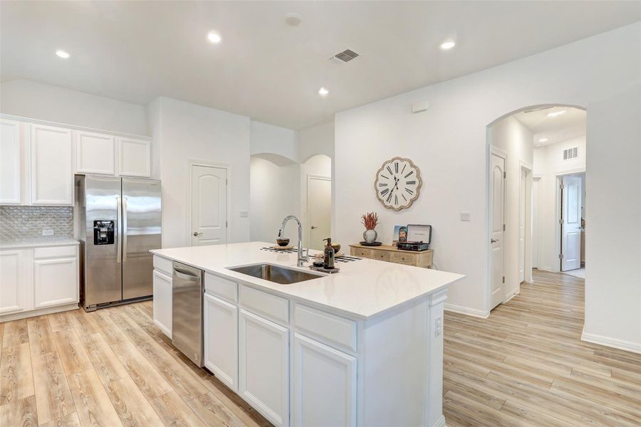 Kitchen with stainless steel appliances, arched walkways, light wood-style floors, a center island with sink, and recessed lighting