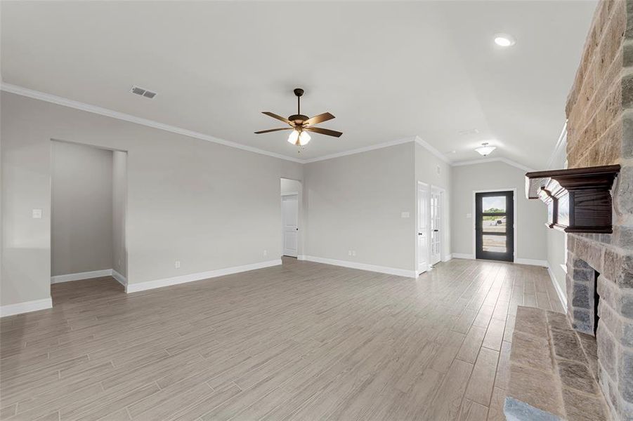 Unfurnished living room featuring crown molding, light wood finished floors, ceiling fan, a fireplace, and vaulted ceiling