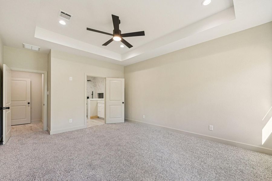 Another view of the spacious primary bedroom showcases neutral tones, recessed lighting, a modern ceiling fan.