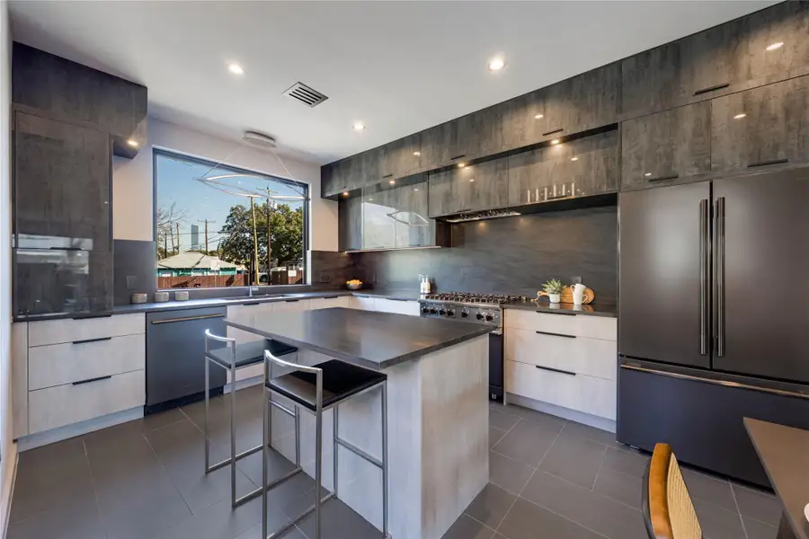 Kitchen featuring modern cabinets, high end appliances, a kitchen breakfast bar, decorative backsplash, and black tile.