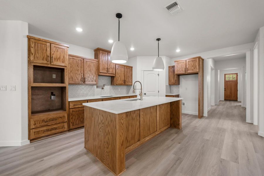 A generously sized kitchen island with pristine white countertops serves as the focal point in this open-concept culinary space. A generously sized kitchen island with pristine white countertops serves as the focal point in this open-concept culinary space.
