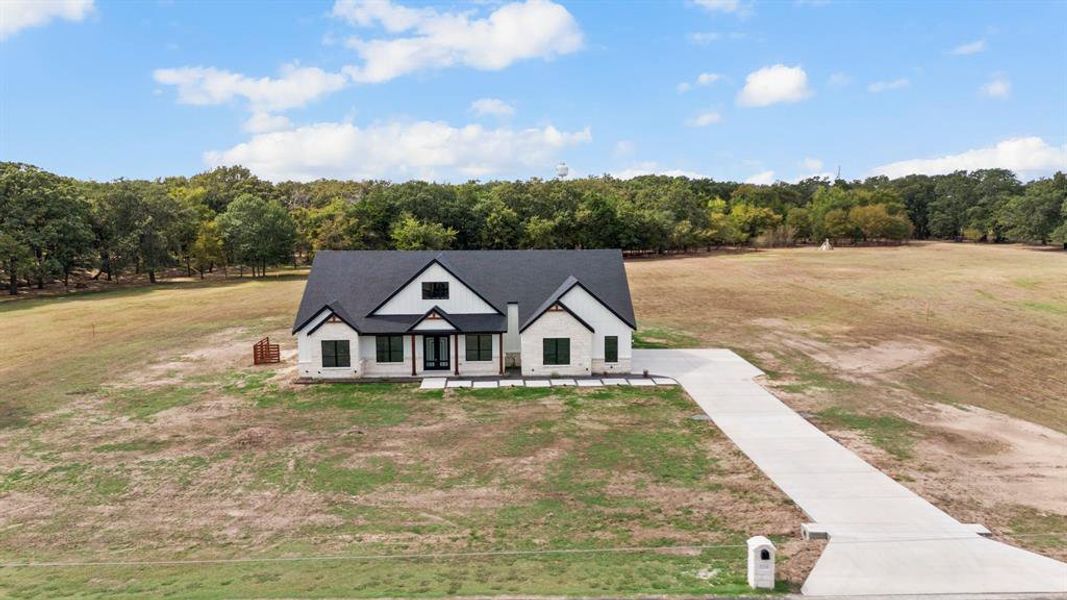 View of front of property featuring a front lawn, stone siding, and a forest view