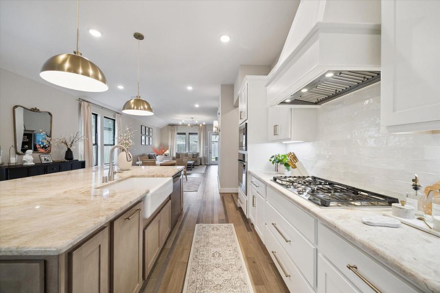Upgraded chef’s kitchen features a 36" five-burner gas cooktop, vent hood, and ample counter space framed by glossy tile backsplash and quartzite countertops.