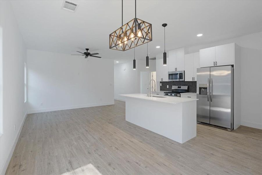 Kitchen with pendant lighting, a kitchen island with sink, sink, ceiling fan, and appliances with stainless steel finishes