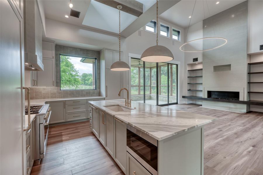 Kitchen with a sink, built in appliances, light wood-style floors, light stone counters, and a kitchen island with sink