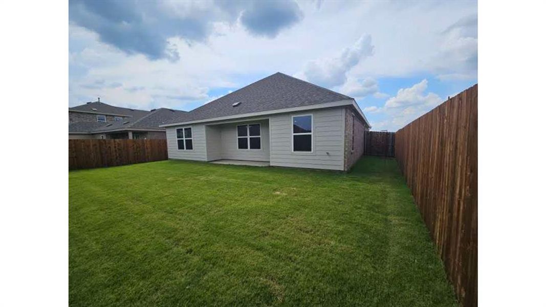 Expansive backyard featuring a large green lawn, full wood privacy fencing, a covered patio, and light-colored siding