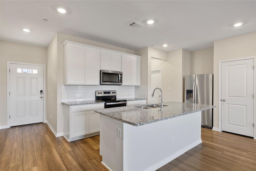 Kitchen featuring stainless steel appliances, white cabinetry, decorative backsplash, light stone counters, and a kitchen island with sink Kitchen featuring stainless steel appliances, white cabinetry, decorative backsplash, light stone counters, and a kitchen island with sink