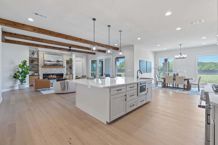 Kitchen featuring light wood-style floors, beamed ceiling, a fireplace, a center island with sink, and decorative light fixtures