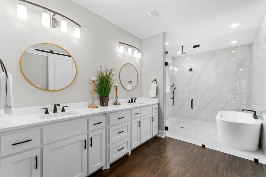 Full bathroom featuring a marble finish shower, double vanity, a freestanding bath, wood finished floors, and recessed lighting Full bathroom featuring a marble finish shower, double vanity, a freestanding bath, wood finished floors, and recessed lighting