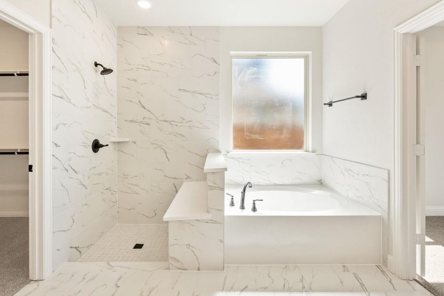 Master bathroom with marble tile walls, walk-in shower with bench, and soaking tub near frosted window