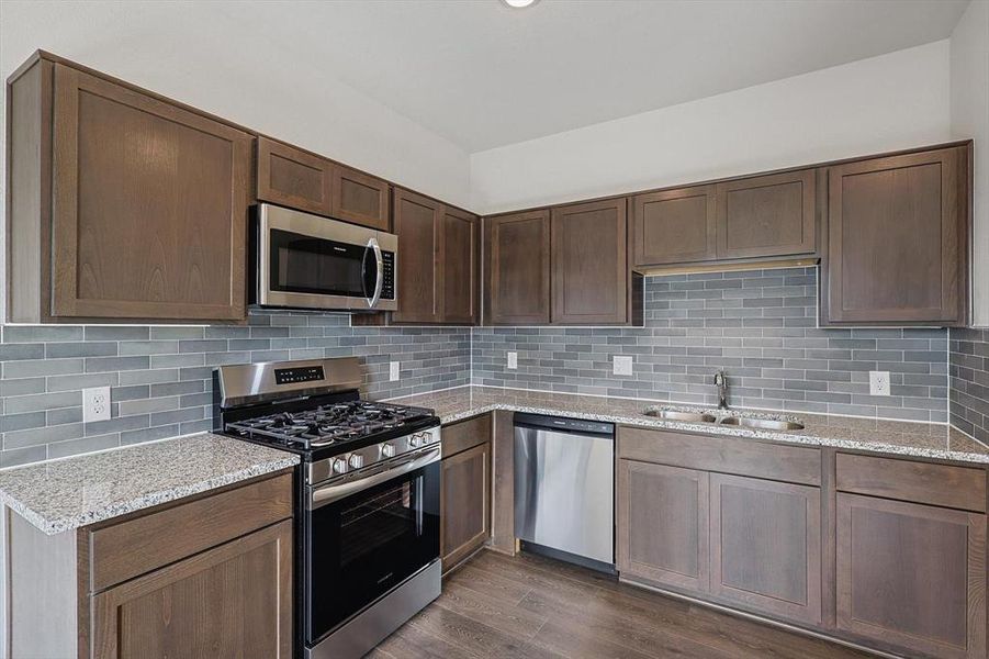 Kitchen featuring sink, backsplash, dark hardwood / wood-style floors, stainless steel appliances, and light stone countertops