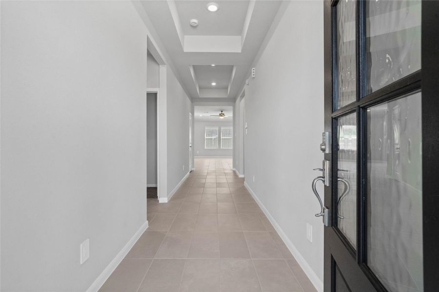 This entryway features a modern, open-concept design. The bright, wide corridor utilizes a neutral color palette, recessed lighting, tray ceilings, and durable tile flooring to lead the eye toward the home's main living area.