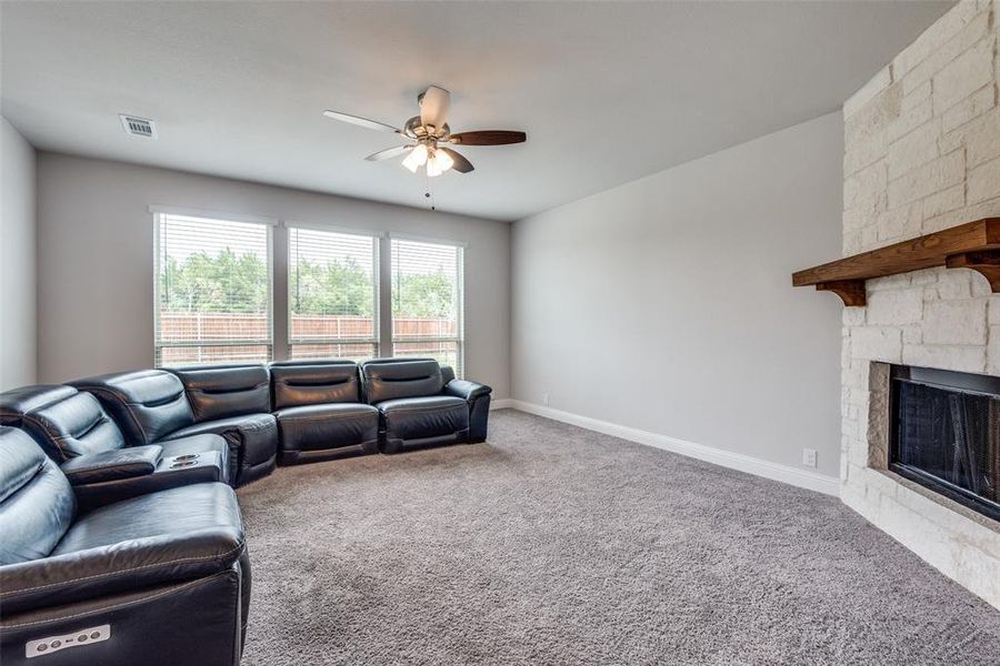 Living room featuring ceiling fan, a stone fireplace, and carpet