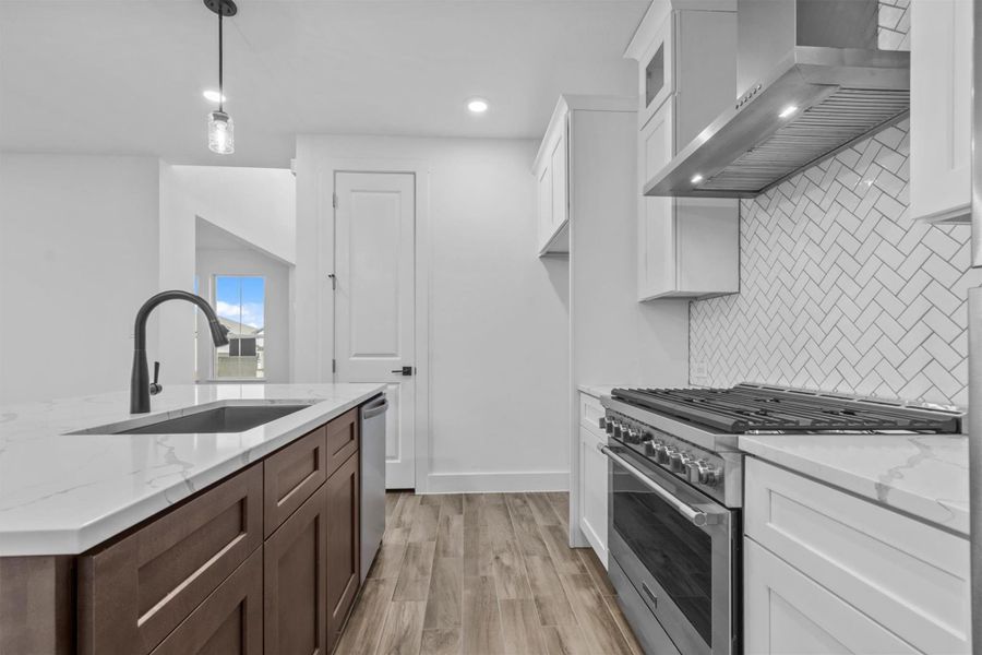 Kitchen featuring appliances with stainless steel finishes, wall chimney range hood, pendant lighting, white cabinets, and sink