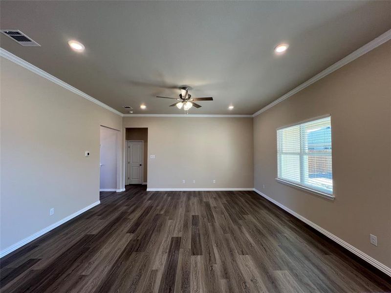 Empty Living room view from kitchen island featuring ceiling fan, dark wood-type flooring, and ornamental molding