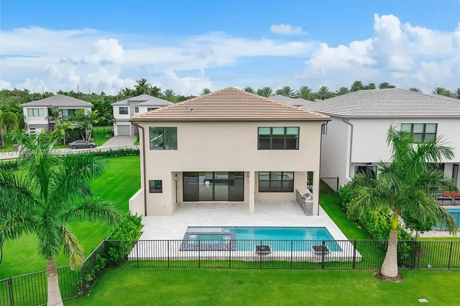 Rear exterior featuring a covered patio, built-in outdoor kitchen, in-ground swimming pool with spa, and fenced-in lawn area