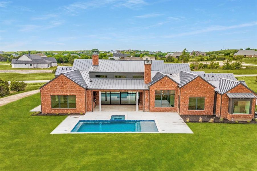 Back of property featuring a standing seam roof, brick siding, a patio, and a lawn
