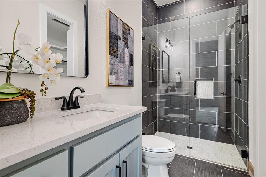 Bathroom featuring vanity, quartz counters, framed mirror, tile floors, frameless glass shower