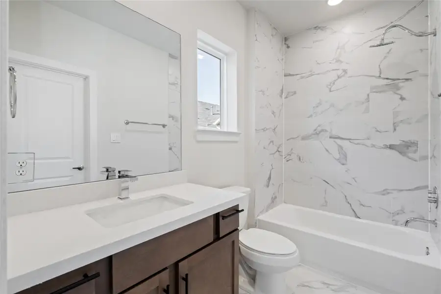 Secondary bath with a full tub-shower wrapped in large format marble-look tile — a finish you don't usually see at this level. Secondary bath with a full tub-shower wrapped in large format marble-look tile — a finish you don't usually see at this level.