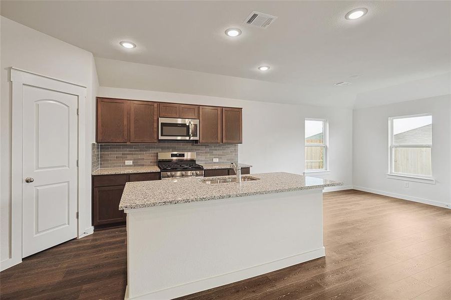 Kitchen with appliances with stainless steel finishes, dark hardwood / wood-style floors, sink, and an island with sink