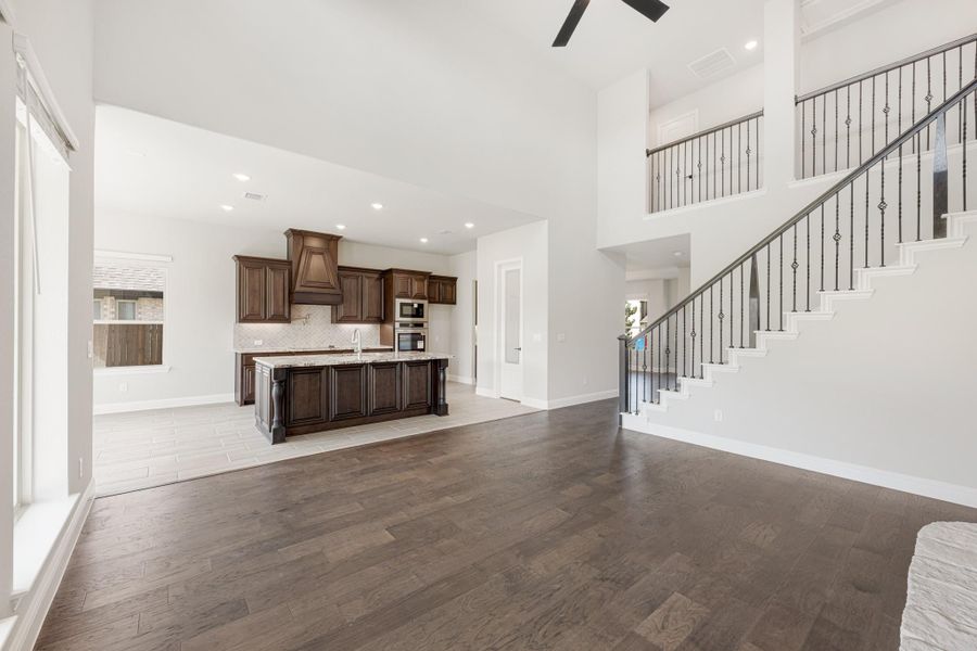 Open living area with dark hardwood floors, staircase with iron balusters, and kitchen with dark wood cabinets and island. Open living area with dark hardwood floors, staircase with iron balusters, and kitchen with dark wood cabinets and island.