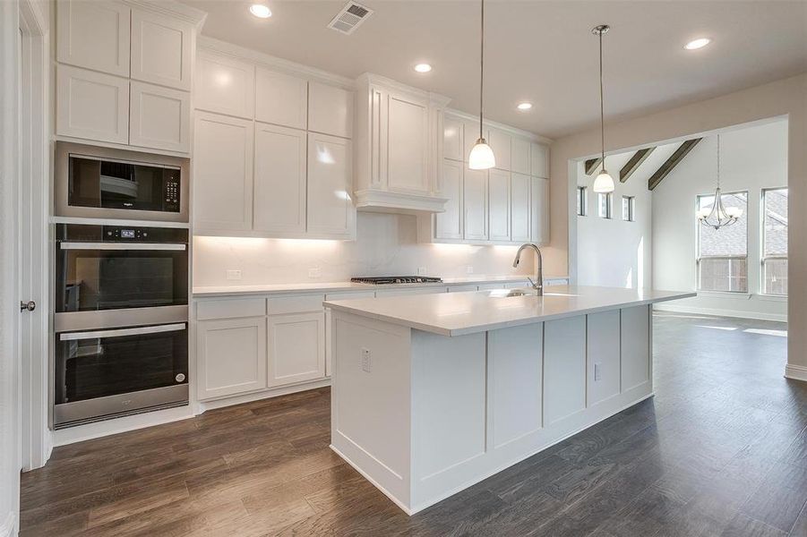 Kitchen featuring white cabinets, appliances with stainless steel finishes, a kitchen island with sink, and dark wood-type flooring