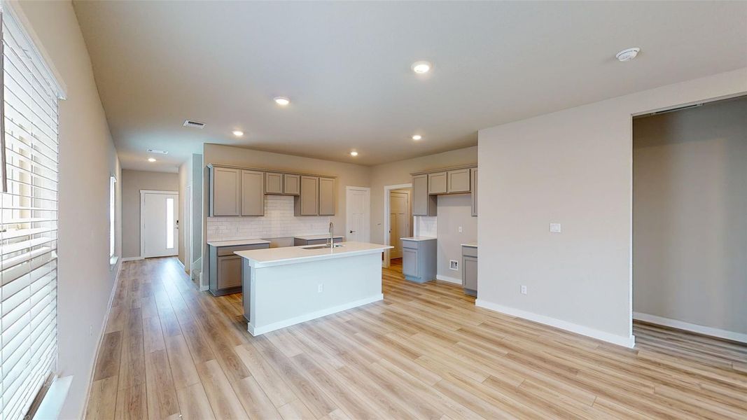 Kitchen featuring a kitchen island with sink, light wood finished floors, recessed lighting, gray cabinets, and tasteful backsplash