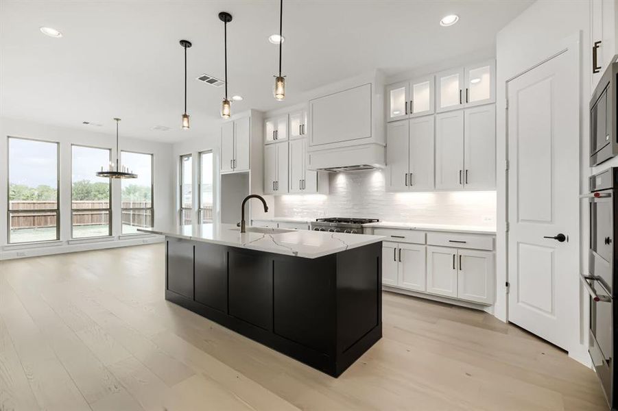 Two tone kitchen with light wood-type flooring, an island with sink, light stone countertops, two tone color scheme, and decorative backsplash
