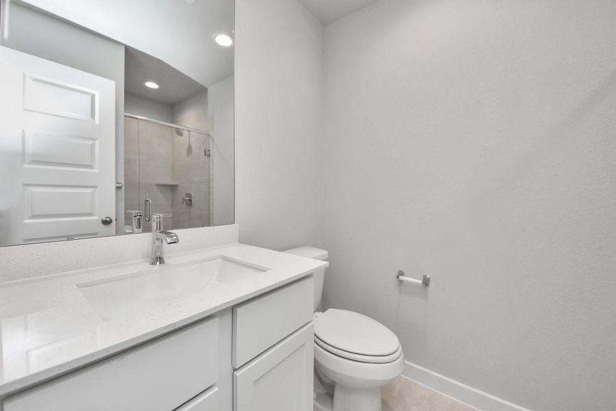 Secondary bath features tile flooring, walk-in shower with tile surround, light stained wood cabinets, beautiful light countertop.