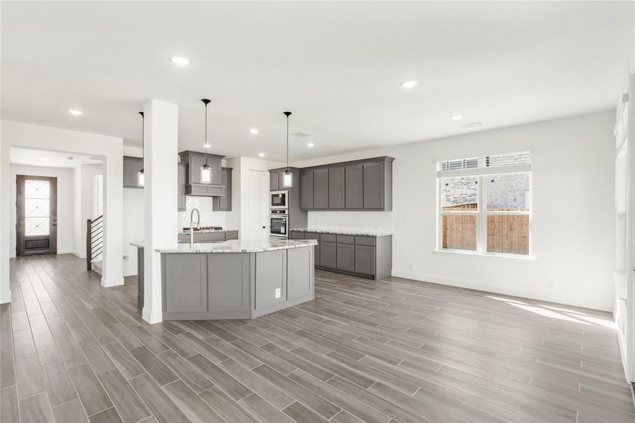 Open-concept kitchen with gray cabinets, curved island, pendant lights, and wood-look tile floors Open-concept kitchen with gray cabinets, curved island, pendant lights, and wood-look tile floors