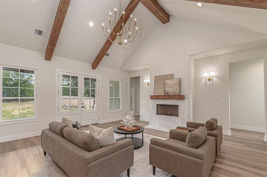 Spacious living area featuring a vaulted ceiling with exposed wood beams, a central chandelier, and wood-finish flooring