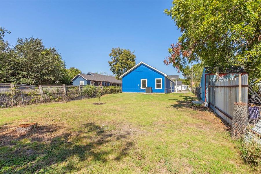 Expansive backyard featuring a manicured lawn, established trees, and a chain-link fence