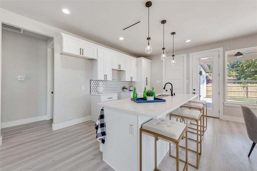 Kitchen with light hardwood / wood-style flooring, a kitchen island with sink, hanging light fixtures, and white cabinetry