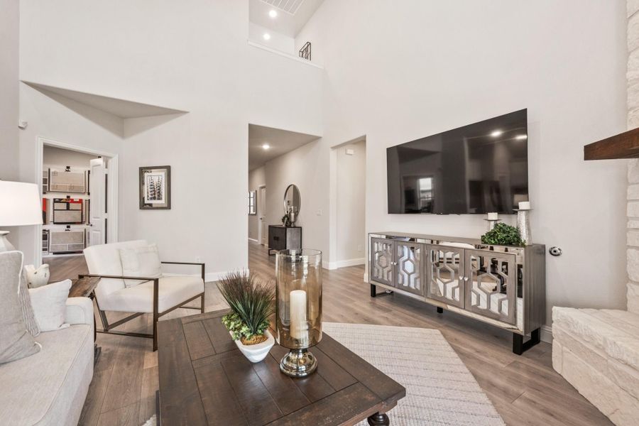 Living room with two-story ceiling, hardwood floors, wall-mounted TV, and stone fireplace surround Living room with two-story ceiling, hardwood floors, wall-mounted TV, and stone fireplace surround