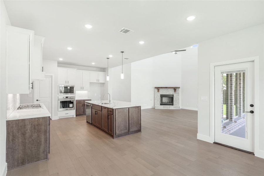 Open-concept kitchen with dark wood island, white cabinets, stainless appliances, and living area with stone fireplace and hardwood floors. Open-concept kitchen with dark wood island, white cabinets, stainless appliances, and living area with stone fireplace and hardwood floors.
