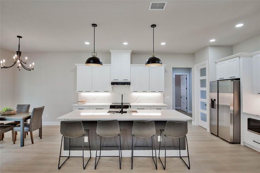 Kitchen featuring white cabinetry, pendant lighting, stainless steel refrigerator with ice dispenser, a breakfast bar, and light wood-style flooring Kitchen featuring white cabinetry, pendant lighting, stainless steel refrigerator with ice dispenser, a breakfast bar, and light wood-style flooring