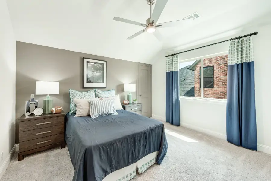 Bedroom with blue bedding, ceiling fan, carpet floors, and window with blue curtains