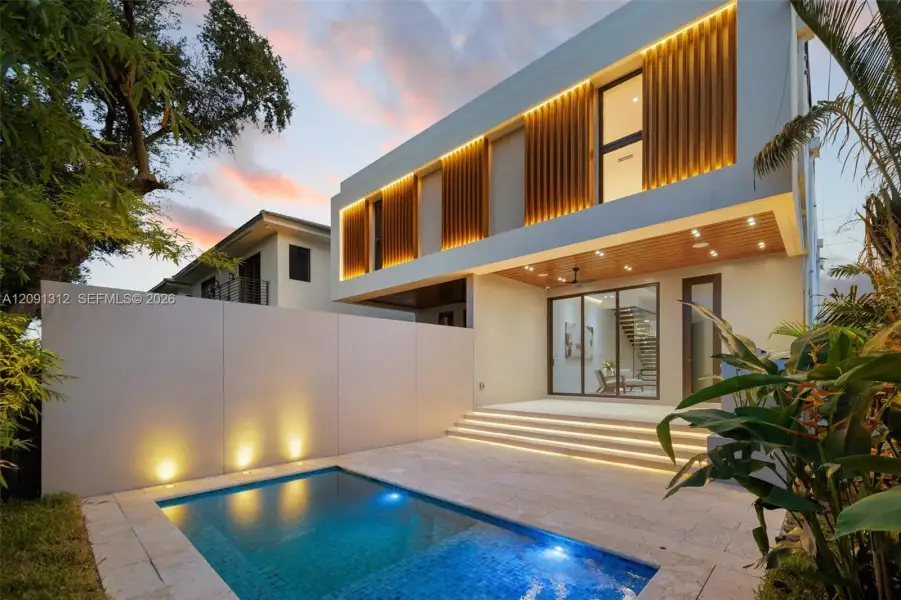 Modern architectural exterior featuring vertical wood-slat detailing, recessed integrated lighting, a stone-surround swimming pool, and a raised concrete patio with tiered steps Modern architectural exterior featuring vertical wood-slat detailing, recessed integrated lighting, a stone-surround swimming pool, and a raised concrete patio with tiered steps