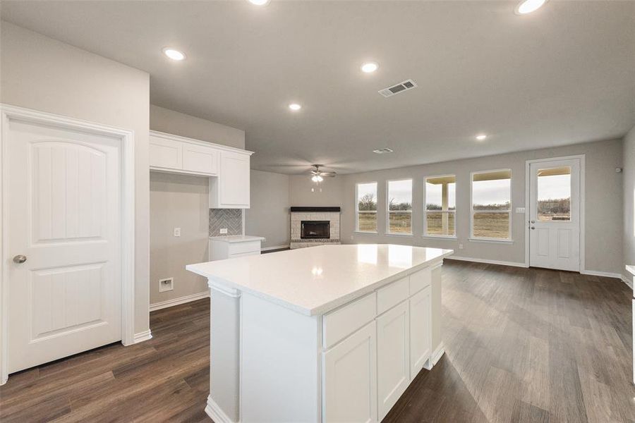 Kitchen featuring a kitchen island, open floor plan, white cabinetry, a brick fireplace, and recessed lighting